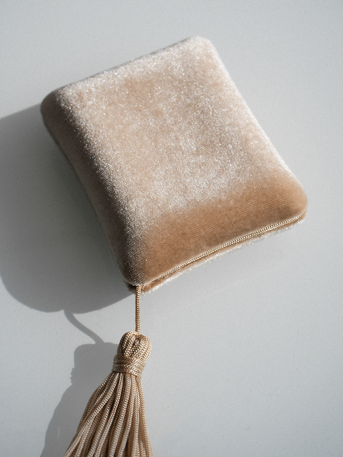 Beigefarbenes Goddess Jewelry Case aus Seidensamt mit dekorativer Quaste und goldener Kette auf einem Samtkissen.